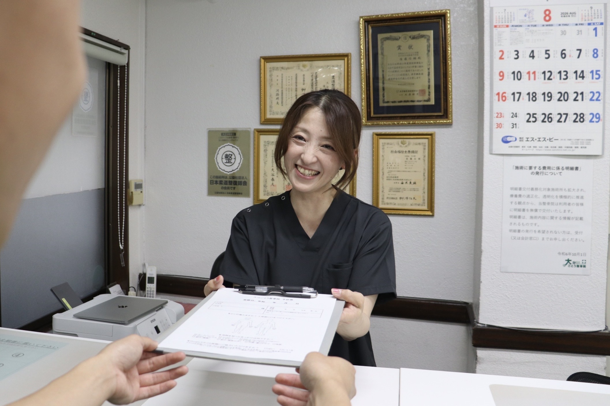 大分ごとう整骨院の女性セラピスト 渡邉敦子先生｜受付で問診票を渡している